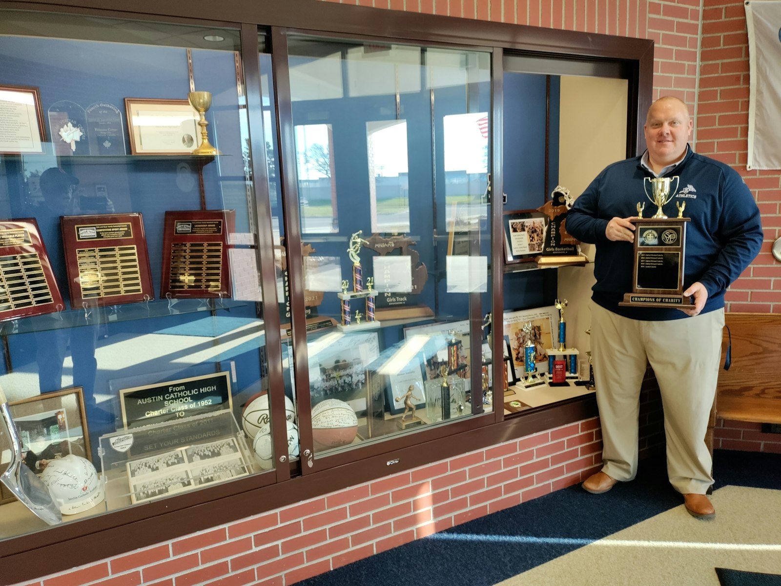 Austin assistant principal and athletic director Jim Baker holds the “Champions of Charity” trophy that has occupied the Austin Catholic trophy case since the school won the award in 2019. When the Catholic League decided to not sponsor the clothing drive this year, Austin went on its own to fill a truckload for the Society of St. Vincent de Paul. (Photo by Don Horkey | Special to Detroit Catholic)