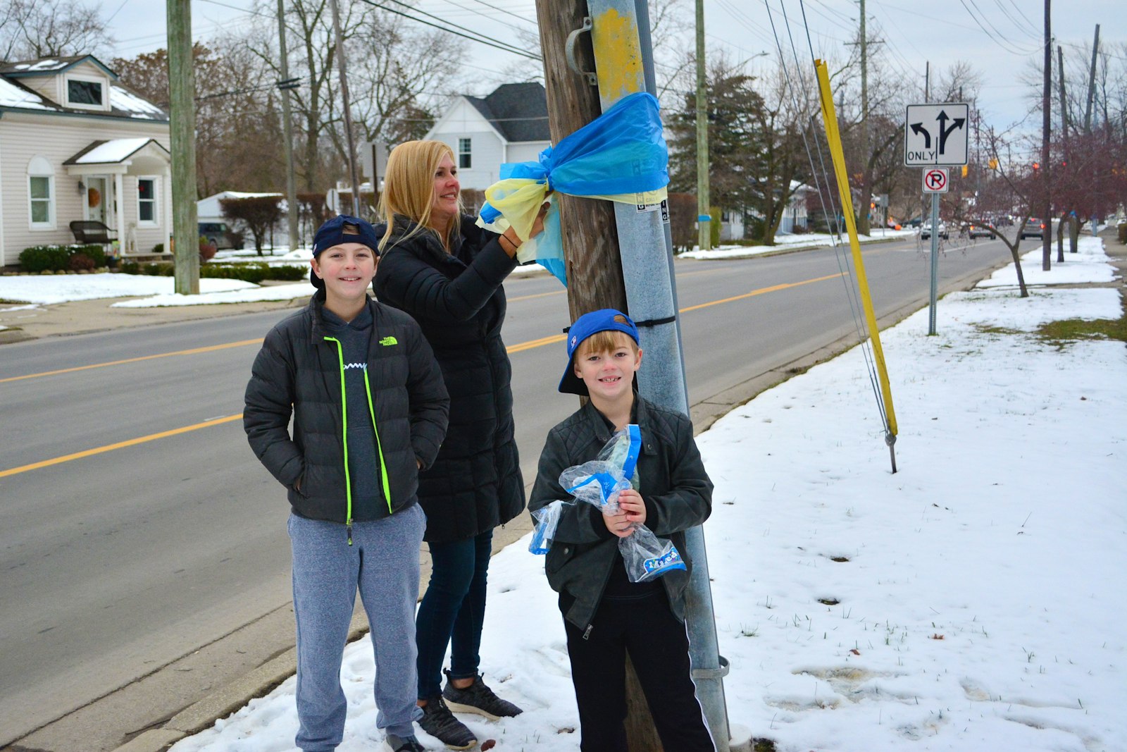 A woman and two boys, who chose not to be identified, tie blue and gold ribbons to telephone poles along Glaspie Street near Oxford High School on Dec. 1. Dozens of volunteers hung banners, ribbons and signs throughout the town.